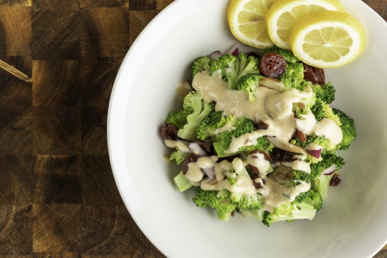 Crunchy Broccoli Salad made with WayFare Dairy Free Sour Cream served in a dinner bowl with lemons on the side.
