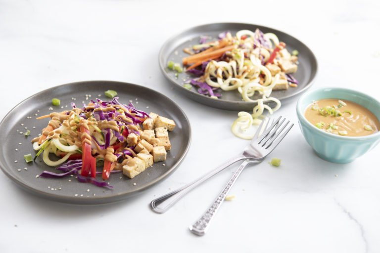 Two plates of Rainbow Raw Thai Salad topped with creamy garlic dressing using WayFare Dairy Free Sour Cream.