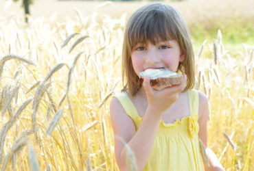 A little kid in a tall, grassy field eating a piece of toast with WayFare's Butter.