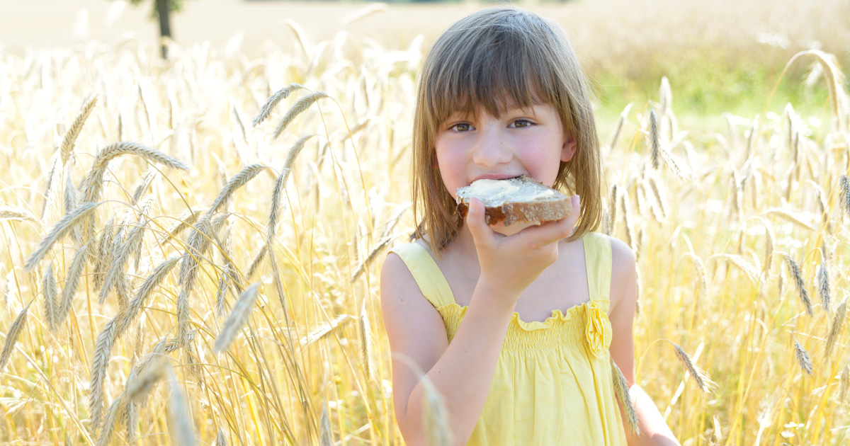 A little kid in a tall, grassy field eating a piece of toast with WayFare's Butter.